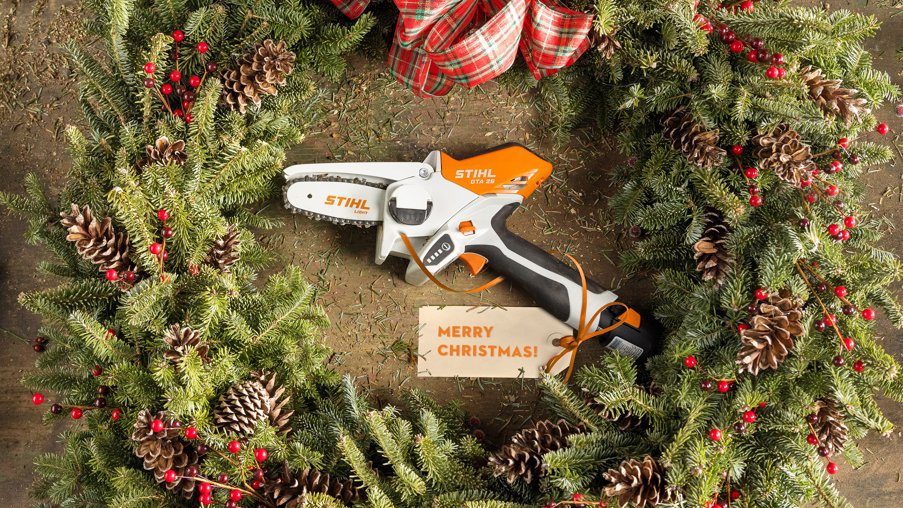 STIHL GTA 26 tool presented in a holiday wreath, surrounded by greenery, pinecones, and a holiday ribbon, with christmas card