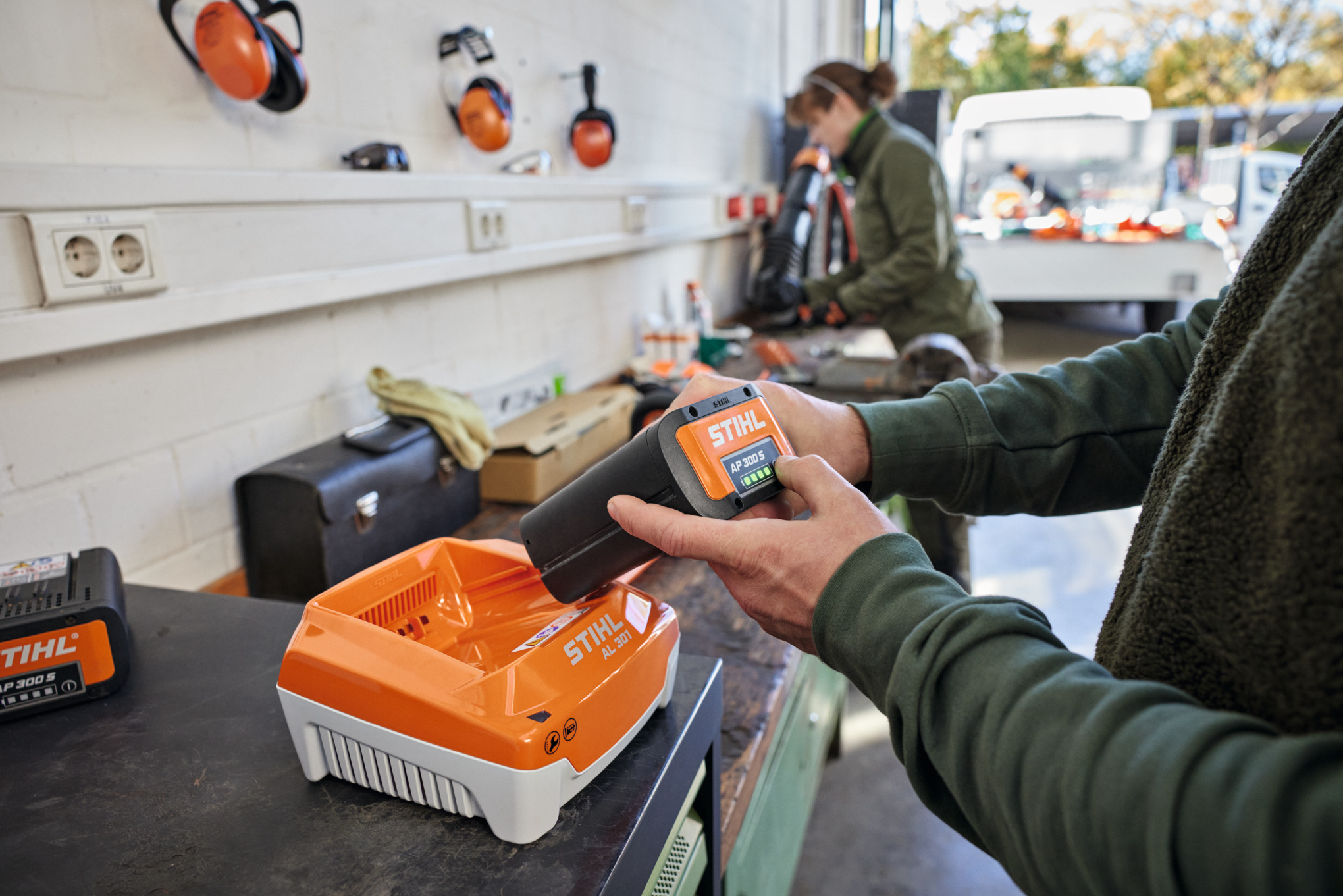 One person inserts a STIHL AP 300 S battery into a STIHL AL 301 quick charger.