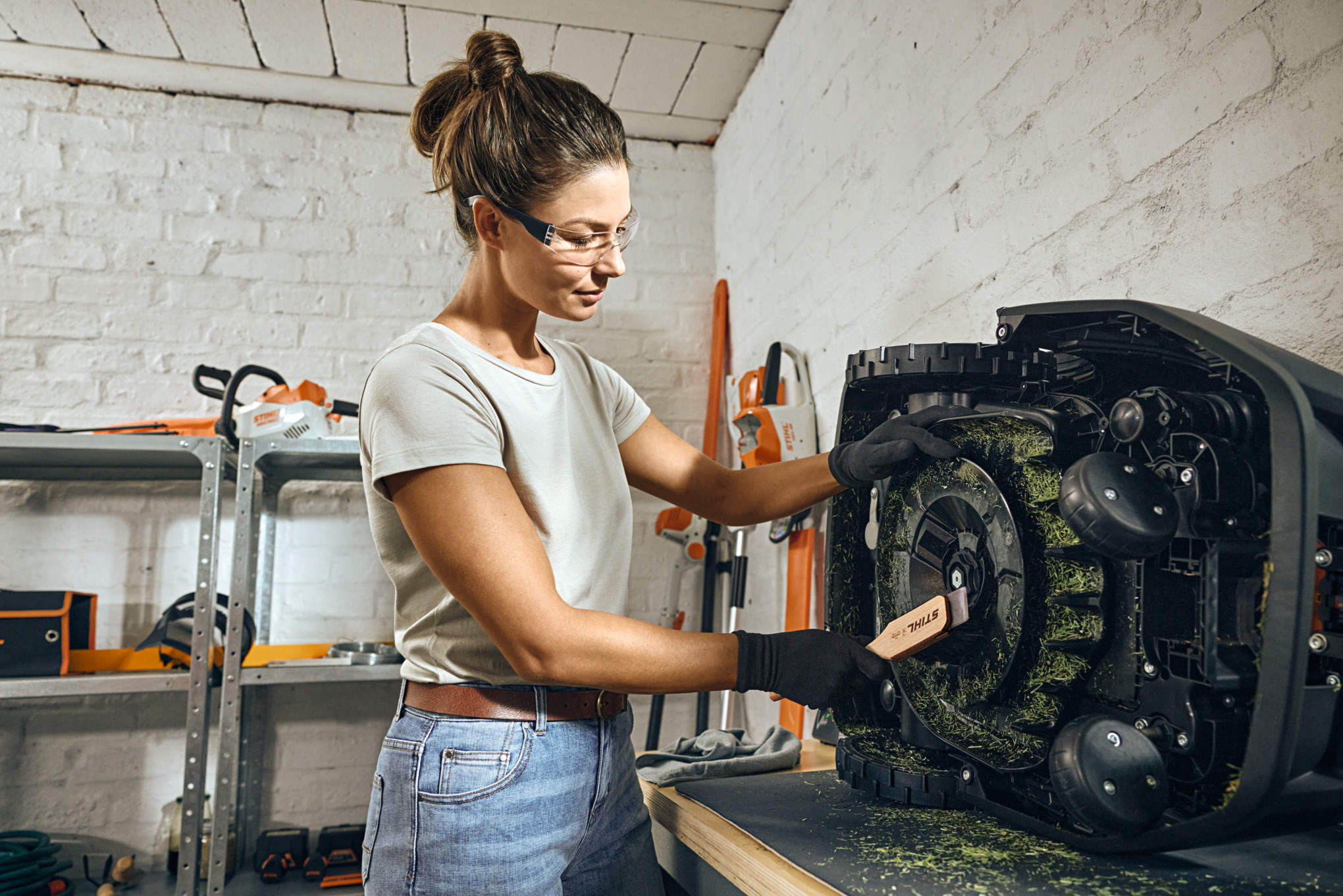A STIHL iMOW® robot lawn mower turned on its side ready for cleaning, with a brush on the ground nearby